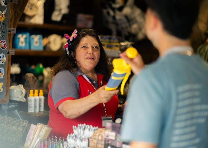 Une conseillère vendeuse remet un produit à un client dans une boutique du Parc Astérix.
