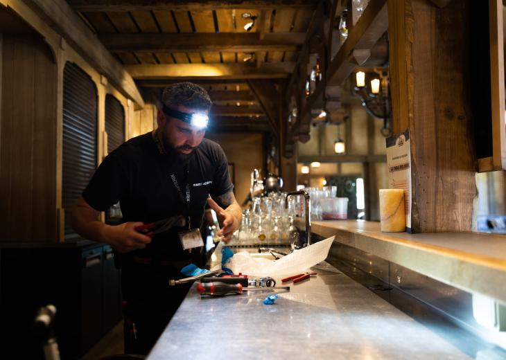 Un technicien de maintenance répare une installation de plomberie derrière le bar d’un restaurant du Parc Astérix.